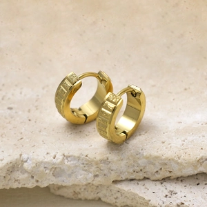 Macro detail of golden hoop earrings with frosted texture and geometric gear grooves
