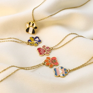 Detailed view of five colorful enamel cat paw pendant necklaces on cream satin fabric