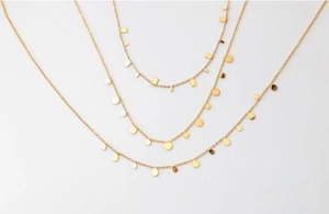 Detailed view of layered gold necklaces with geometric bar, round, and teardrop pendants