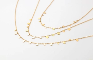 Detailed view of three minimalist gold necklaces with geometric charm pendants on white background