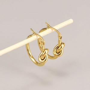 Detalle de pendientes de aro dorados con nudo mostrados sobre una vara de madera
