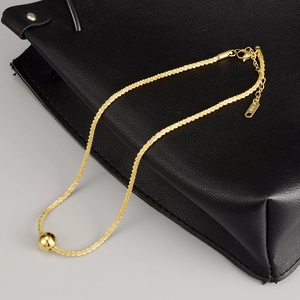 Polished gold ball pendant on a textured K18 titanium steel necklace over a black leather bag