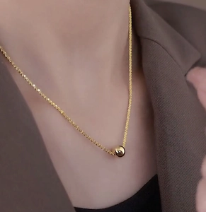 Detailed close-up of a high-polished gold ball pendant on a delicate titanium steel chain