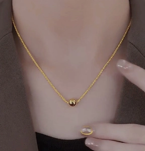 Close-up of golden stainless steel ball pendant necklace with sparkling textured chain