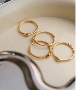 Nahaufnahme von vier organischen 18K Goldstapelringen mit Lavatropfen-Details in einer Schale