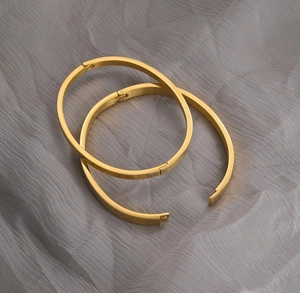 Minimalist 18K gold plated titanium steel bangles on elegant gray fabric backdrop