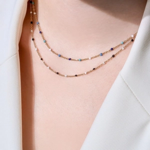 Collar de doble capa dorada con cuentas de colores en una modelo con un traje blanco