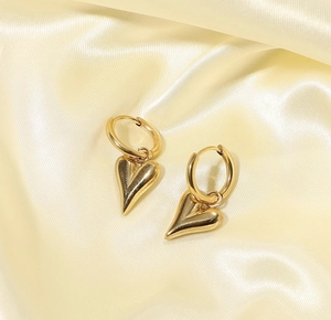 Polished gold stainless steel heart pendant earrings on soft silk background