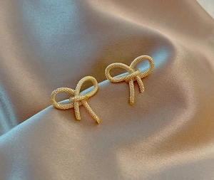 Boucles d'oreilles nœud dorées 18K avec texture torsadée sur fond de satin de soie chic