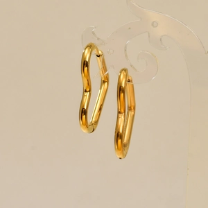 Détail de boucles d'oreilles cœur dorées irrégulières sur un support acrylique