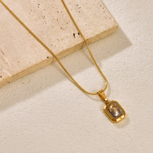 Detail view of gold snake chain necklace with rectangular emerald stone pendant