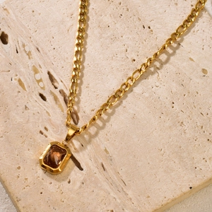 18k gold emerald-cut brown gemstone pendant necklace with figaro chain on stone surface