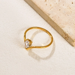Macro shot of V-shaped gold ring featuring a pear-cut zircon on beige stone texture