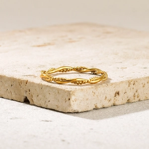 Detail eines minimalistischen goldenen Kordelrings auf einem strukturierten Steinsockel