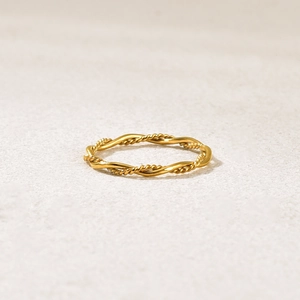 Minimalistischer doppellagiger goldener Kordelring für Damen auf Steinoberfläche