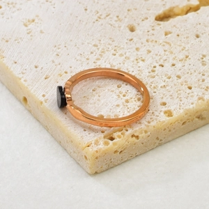 Close-up of rose gold ring with black heart charm on beige textured stone surface