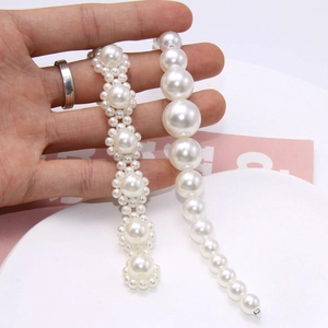 Macro shot of faux pearl shoe chains and jewelry being held against a minimalist background