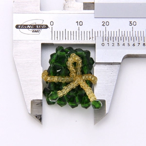 Close-up of green and yellow beaded triangle dumpling charm measured with a caliper