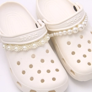Close-up of white garden clogs featuring elegant faux pearl chain charm accessories