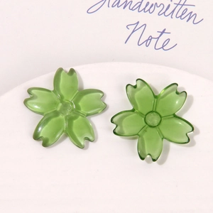 Macro shot of two translucent green cherry blossom resin charms on a white ceramic tray