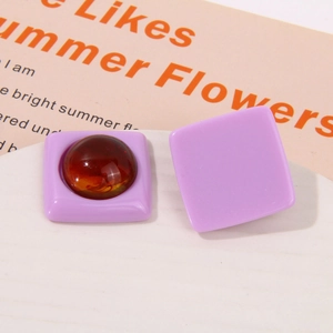 Detailed view of square resin earring charms with amber bead inlay on a white tray