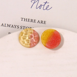 Detail of round resin stud earrings with hammered metal texture and glitter finish