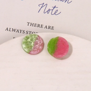 Close-up of pink and green resin earrings with hammered texture on white platform