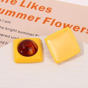 Close-up of yellow resin square earrings with amber-patterned round inlay on white stand