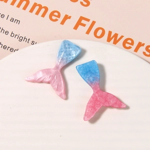 Detailed macro view of gradient glitter resin mermaid tail charms on white tray