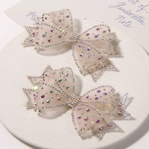 Detailed view of two champagne mesh bow hair clips with shimmering rhinestones in a ceramic tray