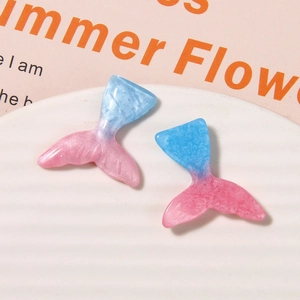 Detail shot of two gradient resin mermaid tail charms with glitter on a white tray