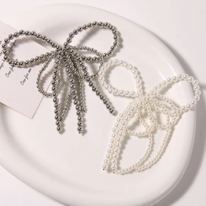 Detail of elegant pearl and silver bead bow charms with tassels on a white tray