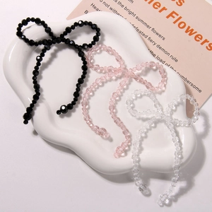 Handmade beaded crystal bow charms in black, pink, and clear colors on a ceramic plate