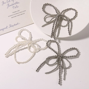 Elegant beaded bow hair clips with white pearls and silver metal beads on a ceramic plate