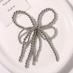 Detail of a silver beaded bow charm with hanging tassels on a white ceramic dish