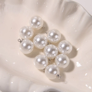 Close-up of polished white round pearl pendants with silver metal loops in a shell bowl