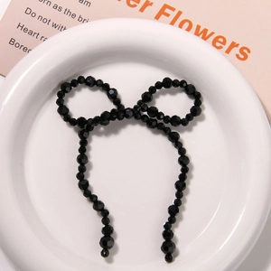 Handmade black beaded bow hair clip accessory displayed on a white ceramic plate