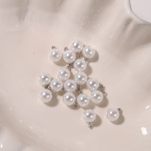 Macro shot of round white pearl pendants with silver loops in a white shell dish