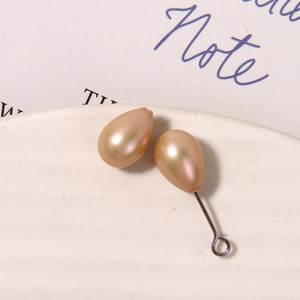 Detail of pear-shaped champagne pearl beads with metal loop in a white ceramic dish
