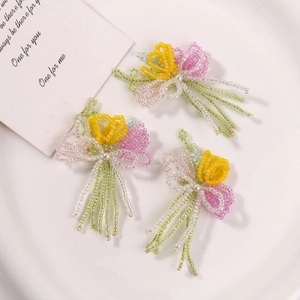 Detail of three handmade beaded tulip flower charms with faux pearls on a ceramic plate