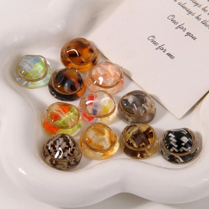 Macro shot of assorted round acetate resin DIY charms with gold wire frames on a ceramic tray
