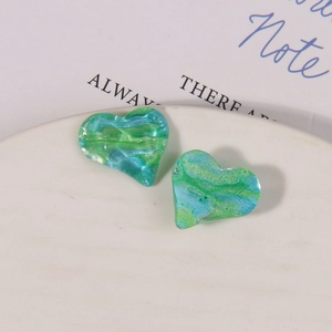 Makroaufnahme von glitzernden blau-grünen Herz-Anhängern mit Marmortextur auf weißem Teller