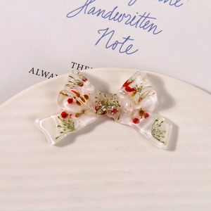 Macro shot of resin bow pendant with dried flowers and white pearl on a ceramic tray