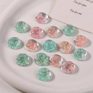 Close-up of clear resin dome cabochons with pink and teal dried flowers on a tray