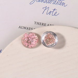Macro detail of handmade clear resin charms with pink dried flowers and silver rim