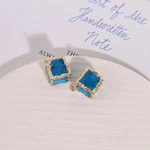 Detailed macro view of irregular square blue charms with textured gold edges for DIY jewelry