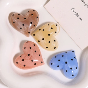 Dettaglio di ciondoli in acetato a forma di cuore con pois neri in quattro colori tenui