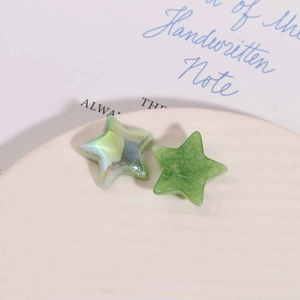 Close-up of pearlized gradient and frosted green resin star charms in a gift tray