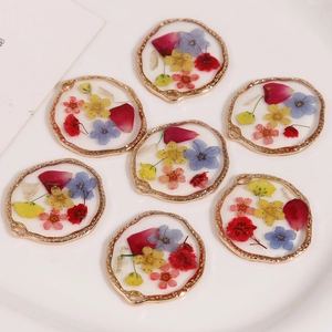 Macro detail of handmade resin charms with dried flowers and gold textured metal alloy frames