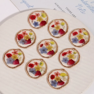 Elegant handmade dried flower resin charms in gold metal frames on a white round tray